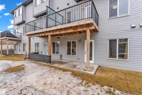 The property features a private balcony with black railings and a glass panel, overlooking a concrete patio area - 32 1703 16 Avenue, Edmonton, AB - Outdoor With Exterior