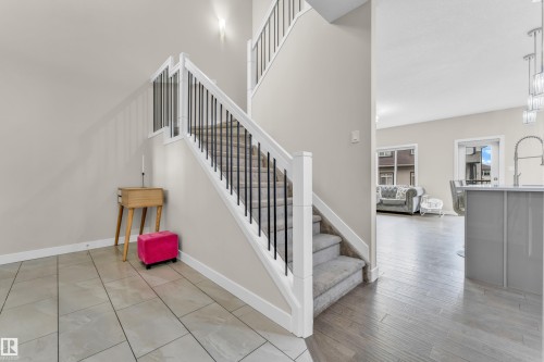 The entryway features tile flooring and a staircase with carpeted treads and a railing with white newel posts and black balusters - 32 1703 16 Avenue, Edmonton, AB - Indoor Photo Showing Other Room