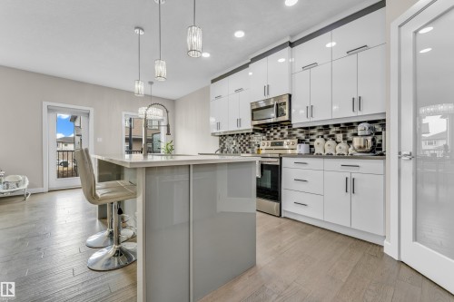 The kitchen features a large island with seating, pendant lighting, stainless steel appliances, and sleek white cabinetry - 32 1703 16 Avenue, Edmonton, AB - Indoor Photo Showing Kitchen With Upgraded Kitchen