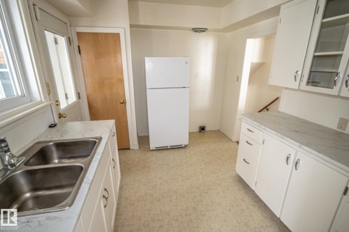 The kitchen features white cabinetry, a double basin stainless steel sink, a refrigerator, and light-colored countertops - 5209 49 Ave, St. Paul Town, AB - Indoor Photo Showing Kitchen With Double Sink