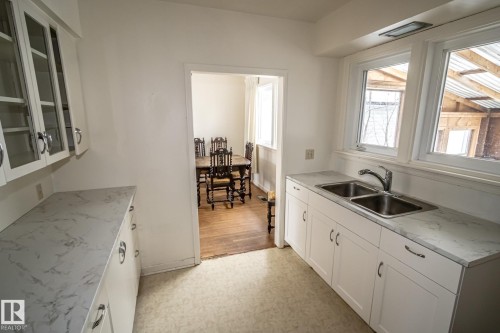 The kitchen features white cabinetry with chrome hardware, a dual basin stainless steel sink, and light-colored countertops - 5209 49 Ave, St. Paul Town, AB - Indoor Photo Showing Kitchen With Double Sink