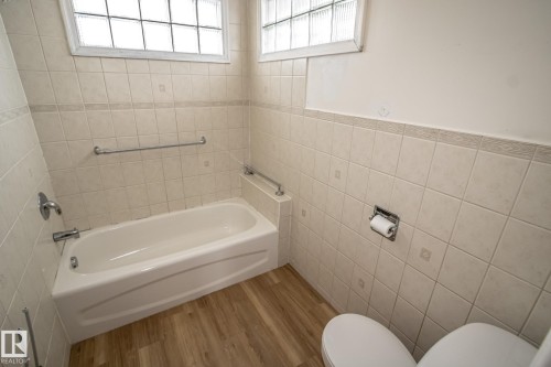 Bathroom featuring a white bathtub, ceramic wall tiles, and wood-look flooring - 5209 49 Ave, St. Paul Town, AB - Indoor Photo Showing Bathroom