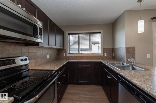 The kitchen features dark wood cabinetry, stainless steel appliances, a double sink, and a tiled backsplash - 1403 Cunningham Drive, Edmonton, AB - Indoor Photo Showing Kitchen With Double Sink