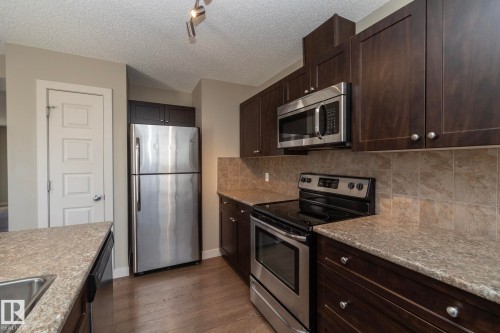 The kitchen features dark wood cabinetry, stainless steel appliances including a refrigerator, range, and microwave, and light-colored countertops with a tiled backsplash - 1403 Cunningham Drive, Edmonton, AB - Indoor Photo Showing Kitchen