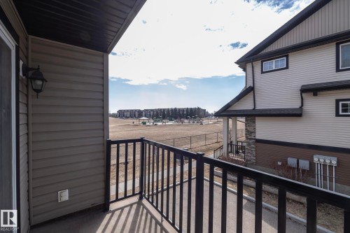 The property includes a private balcony with black railings, offering views of a fenced-in field and distant buildings - 1403 Cunningham Drive, Edmonton, AB - Outdoor With Exterior