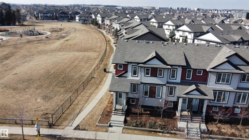 The property features a multi-story design with a gray roof and light-colored siding, and is situated near an expansive green space with a playground - 1403 Cunningham Drive, Edmonton, AB - Outdoor With Facade