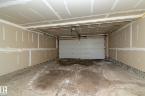 The property includes a garage with a concrete floor, a white garage door, and unfinished drywall on the walls and ceiling - 1403 Cunningham Drive, Edmonton, AB - Indoor Photo Showing Garage