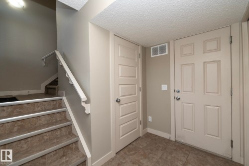 Entryway featuring a tiled floor, two paneled doors, and a staircase with tiled steps and a white handrail - 1403 Cunningham Drive, Edmonton, AB - Indoor Photo Showing Other Room
