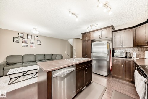 Open concept living area featuring a kitchen island with a double sink, stainless steel appliances, and dark wood cabinetry - 8 13838 166Ave, Edmonton, AB - Indoor Photo Showing Kitchen With Stainless Steel Kitchen