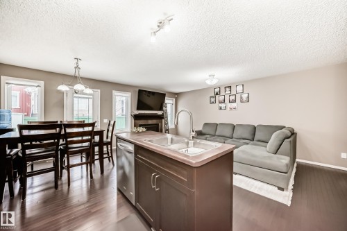 Open concept living space featuring dark hardwood flooring, a central kitchen island with a sink and dishwasher, and a dining area with a chandelier - 8 13838 166Ave, Edmonton, AB - Indoor