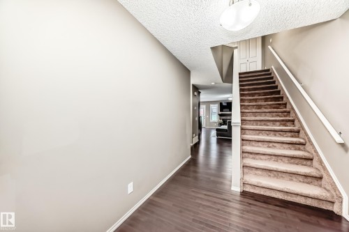 Entryway featuring dark hardwood flooring, a carpeted staircase with a white handrail, and a flush mount light fixture - 8 13838 166Ave, Edmonton, AB - Indoor Photo Showing Other Room
