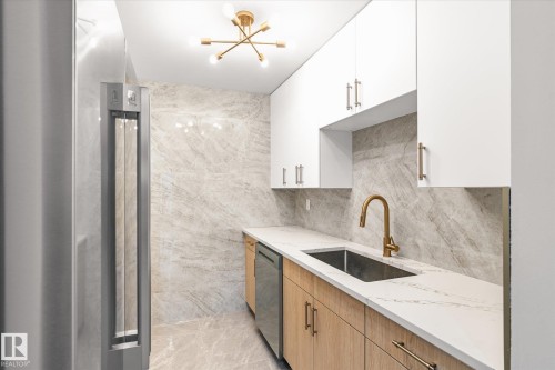 The kitchen features white upper cabinetry, natural wood lower cabinetry, and a white countertop with a sink and a gold-toned faucet - 6540 184 Street, Edmonton, AB - Indoor Photo Showing Kitchen With Upgraded Kitchen