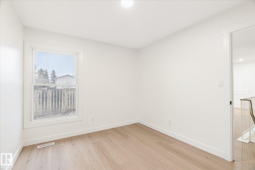 This bright room features a window with a view of external trees and fencing, light-toned flooring, and white walls - 6540 184 Street, Edmonton, AB - Indoor Photo Showing Other Room