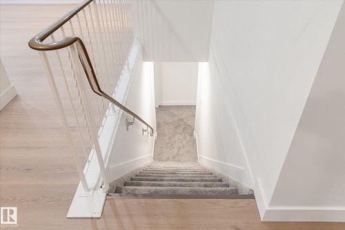 Staircase featuring a light-colored wood floor at the top, a carpeted runner on the stairs, and a metal handrail - 6540 184 Street, Edmonton, AB - Indoor Photo Showing Other Room