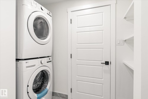Laundry area with stacked washing machine and dryer, white paneled door with black hardware, and built-in shelving - 6540 184 Street, Edmonton, AB - Indoor Photo Showing Laundry Room