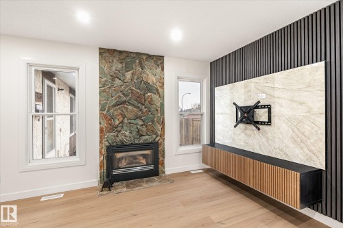Living room featuring hardwood floors, a natural stone fireplace, and two windows - 6540 184 Street, Edmonton, AB - Indoor Photo Showing Living Room With Fireplace