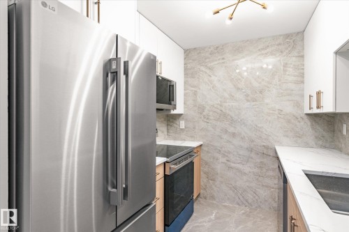 The kitchen features stainless steel appliances, white cabinetry, light wood lower cabinets, and stone-look tile flooring and walls - 6540 184 Street, Edmonton, AB - Indoor Photo Showing Kitchen With Double Sink With Upgraded Kitchen