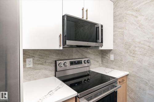Well-appointed kitchen featuring white upper cabinetry, stainless steel appliances, white countertops with natural veining, and a stone-tiled backsplash - 6540 184 Street, Edmonton, AB - Indoor Photo Showing Kitchen