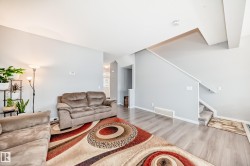 The living area features light-colored walls, a light wood-style floor, and a staircase with a carpeted tread - 