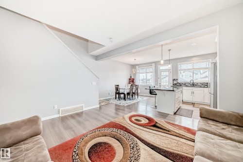 Living area featuring light wood flooring, a partial staircase, and views into the kitchen and dining area - 5868 Anthony Crescent, Edmonton, AB - Indoor Photo Showing Living Room