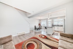 Living area featuring light wood flooring, a partial staircase, and views into the kitchen and dining area - 