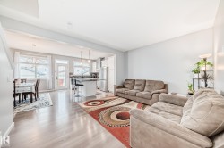 This bright living area features light-toned flooring, a light-colored accent wall, and an open-concept layout leading to the dining area and kitchen - 