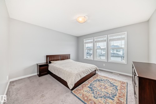 The room features light gray walls, gray carpeting, and three windows providing natural light - 5868 Anthony Crescent, Edmonton, AB - Indoor Photo Showing Bedroom