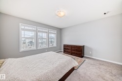 This bedroom offers ample natural light through three large windows, featuring blinds for privacy - 