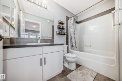Bathroom featuring a white vanity with a dark countertop, a mirror, and a bathtub with a shower - 