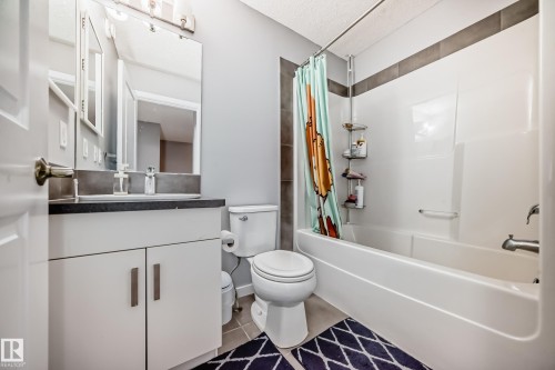 Well-appointed bathroom featuring a vanity with a dark countertop and a white cabinet, a toilet, and a combination shower and bathtub - 5868 Anthony Crescent, Edmonton, AB - Indoor Photo Showing Bathroom