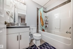 Well-appointed bathroom featuring a vanity with a dark countertop and a white cabinet, a toilet, and a combination shower and bathtub - 