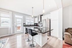 Modern kitchen featuring light wood flooring, white cabinetry, a dark countertop on the kitchen island, stainless steel appliances, and a glass-paneled door leading to the outdoors - 