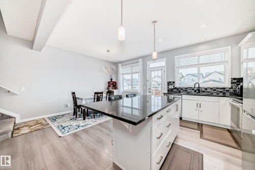 Open concept living space featuring a kitchen island with a dark countertop, white cabinetry with silver hardware, and light-toned flooring - 5868 Anthony Crescent, Edmonton, AB - Indoor Photo Showing Kitchen With Upgraded Kitchen