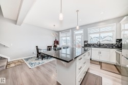Open concept living space featuring a kitchen island with a dark countertop, white cabinetry with silver hardware, and light-toned flooring - 