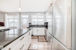 The kitchen features a large island with a dark countertop, white cabinetry with silver hardware, stainless steel appliances, and a dark tile backsplash - 