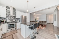 The kitchen features white cabinetry, stainless steel appliances, a dark countertop, and a tiled backsplash - 