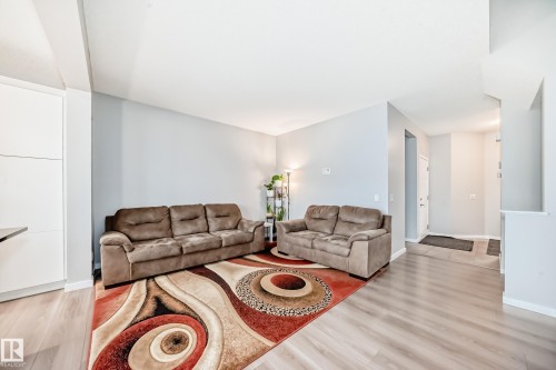 The living area features light-colored walls, light wood-look flooring, and a partial view of a white door - 5868 Anthony Crescent, Edmonton, AB - Indoor Photo Showing Living Room