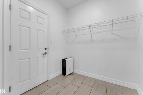 This utility space features a white paneled door, light-colored tiled flooring, and a white wire shelving unit mounted on the wall - 3235 13 Avenue, Edmonton, AB - Indoor