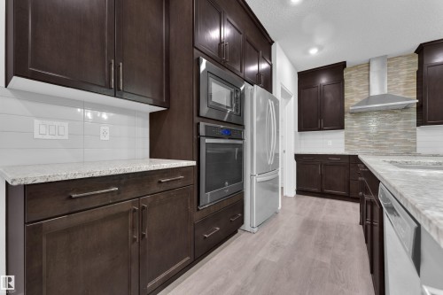 The kitchen features dark wood cabinetry, stainless steel appliances, light-colored countertops, and a subway tile backsplash - 3235 13 Avenue, Edmonton, AB - Indoor Photo Showing Kitchen With Upgraded Kitchen