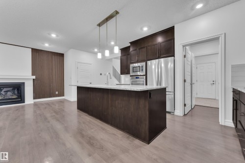 Open concept living space featuring a kitchen island with a light-colored countertop, stainless steel appliances, and a fireplace with a white mantel - 3235 13 Avenue, Edmonton, AB - Indoor Photo Showing Kitchen With Fireplace With Upgraded Kitchen