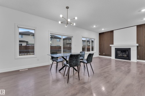 Spacious open concept room featuring light-colored flooring, large windows, a modern fireplace with a white mantel, and dark wood accent wall paneling - 3235 13 Avenue, Edmonton, AB - Indoor With Fireplace