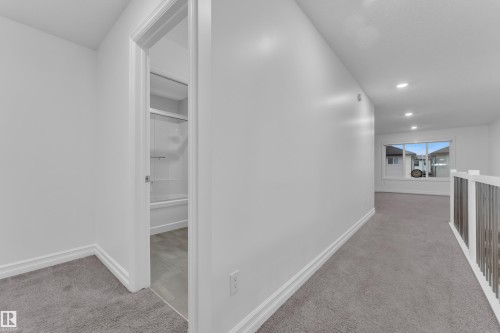 The property features a bright hallway with light grey carpeting, recessed lighting, and a window providing views of the surrounding homes - 3235 13 Avenue, Edmonton, AB - Indoor Photo Showing Other Room