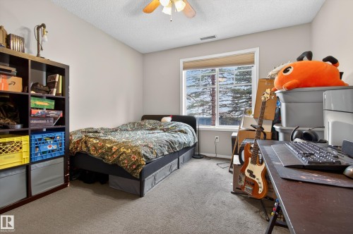 This room features a ceiling fan, a window with a view of trees, and carpeted flooring - 131 2098 Blackmud Creek Drive Sw, Edmonton, AB - Indoor Photo Showing Bedroom