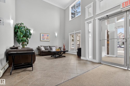 Lobby area featuring high ceilings, light gray walls, large windows, and tiled flooring - 131 2098 Blackmud Creek Drive Sw, Edmonton, AB - Indoor Photo Showing Other Room