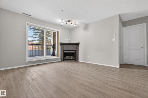 Living area featuring light-toned flooring, a corner fireplace, and a sliding glass door leading to a balcony - 131 2098 Blackmud Creek Drive Sw, Edmonton, AB - Indoor Photo Showing Living Room With Fireplace