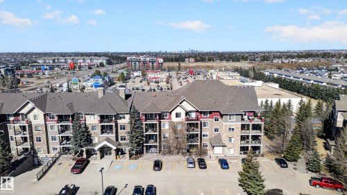 The property features a multi-story building with balconies, a stone and siding exterior, and a spacious parking area - 131 2098 Blackmud Creek Drive Sw, Edmonton, AB - Outdoor With View
