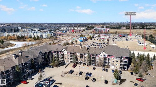 The property features a large parking area and balconies, with a broader view of the surrounding residential and commercial buildings - 131 2098 Blackmud Creek Drive Sw, Edmonton, AB - Outdoor With View