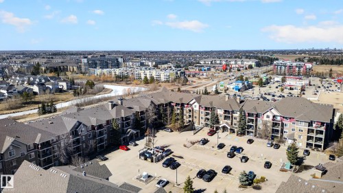 Aerial view showcasing the property's surrounding area, featuring residential buildings, a river, and commercial establishments - 131 2098 Blackmud Creek Drive Sw, Edmonton, AB - Outdoor With View