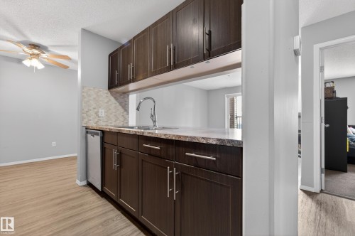 The kitchen features dark wood cabinetry, a stainless steel sink with a high arch faucet, and a light-colored countertop - 131 2098 Blackmud Creek Drive Sw, Edmonton, AB - Indoor Photo Showing Kitchen