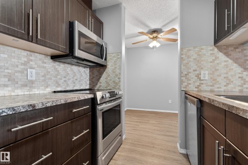 The kitchen features dark wood cabinetry, stainless steel appliances, and a tiled backsplash - 131 2098 Blackmud Creek Drive Sw, Edmonton, AB - Indoor Photo Showing Kitchen With Upgraded Kitchen